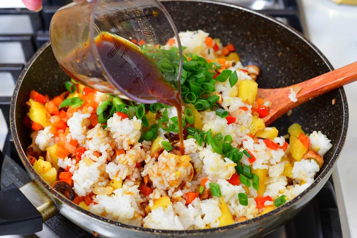 adding sauce to the pan with rice and vegetables
