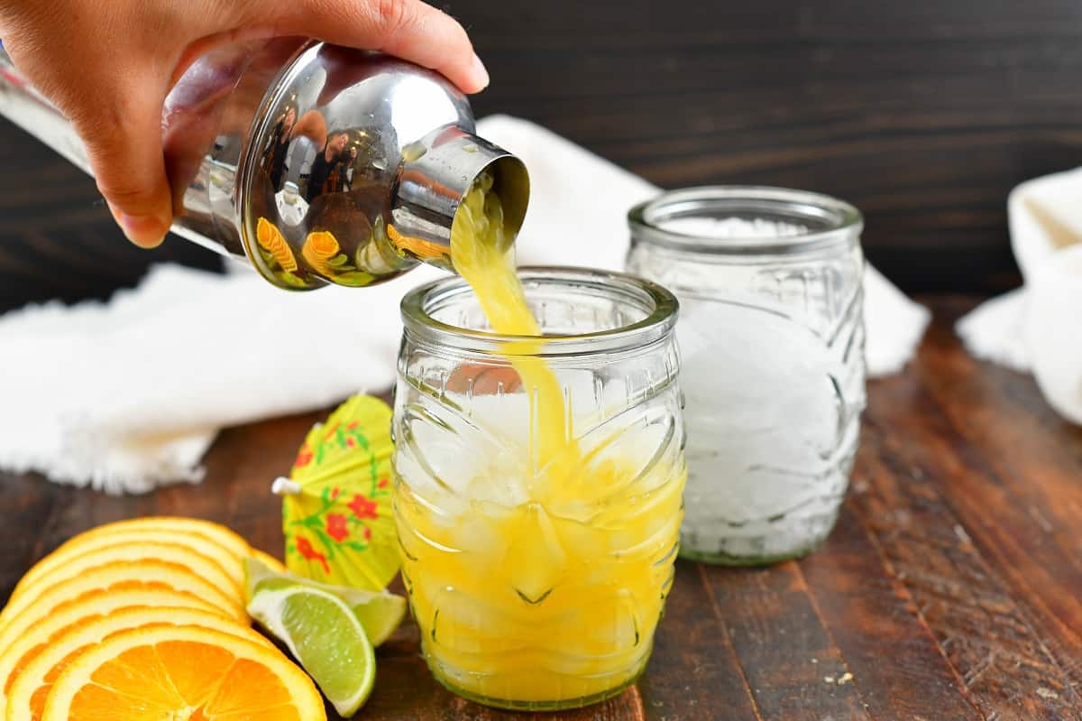 pouring the yellow cocktail into the glass with ice