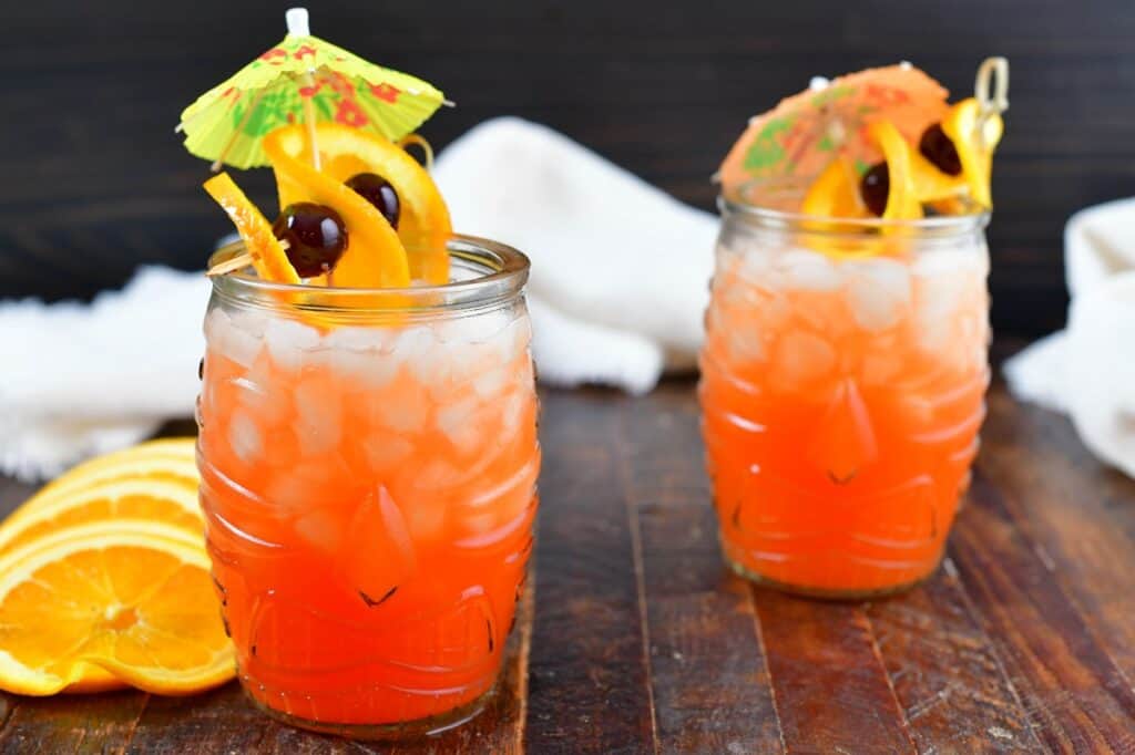 two orange rum cocktails in tiki glasses with garnish