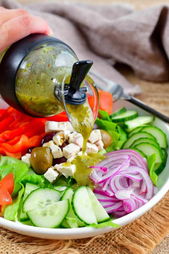 pouring Greek dressing over the salad