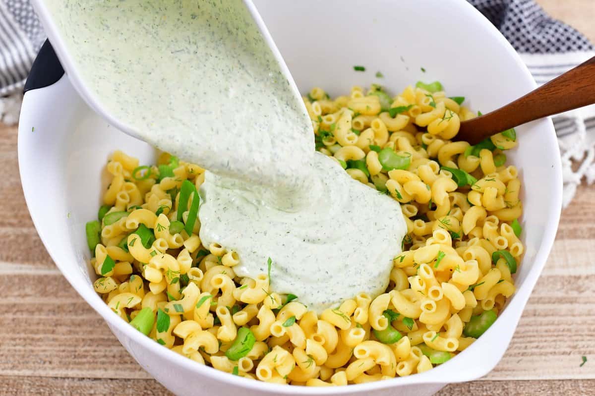 adding green goddess dressing to the pasta in a bowl