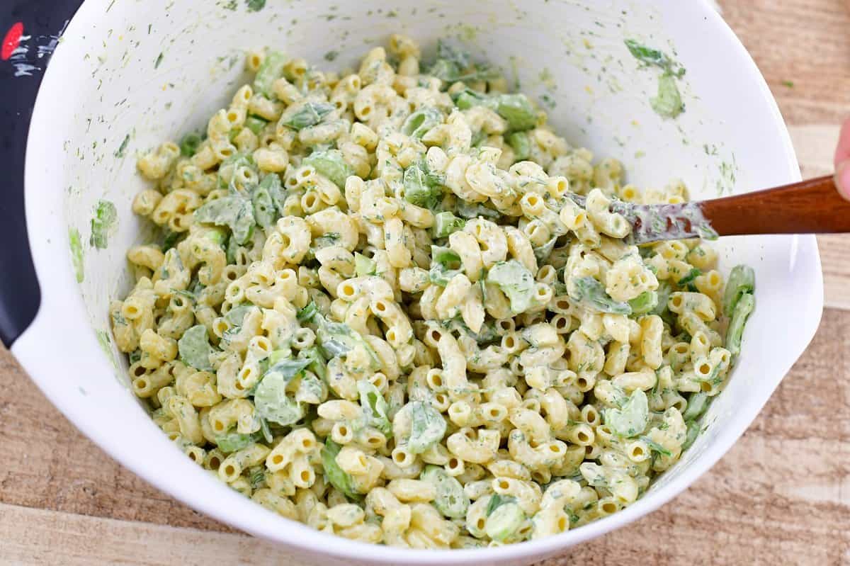 mixing the pasta, veggies, and dressing in a bowl