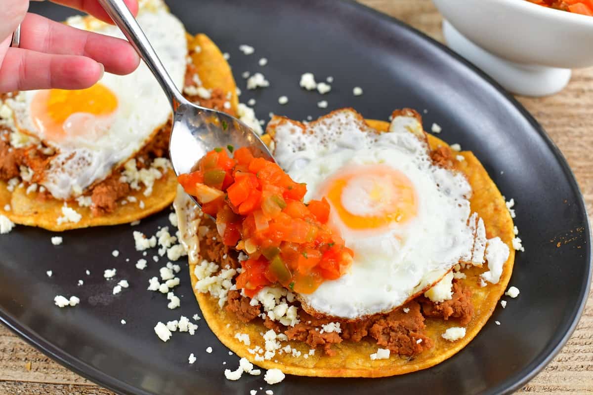 adding tomato sauce to the sunny side eggs over beans and tortilla