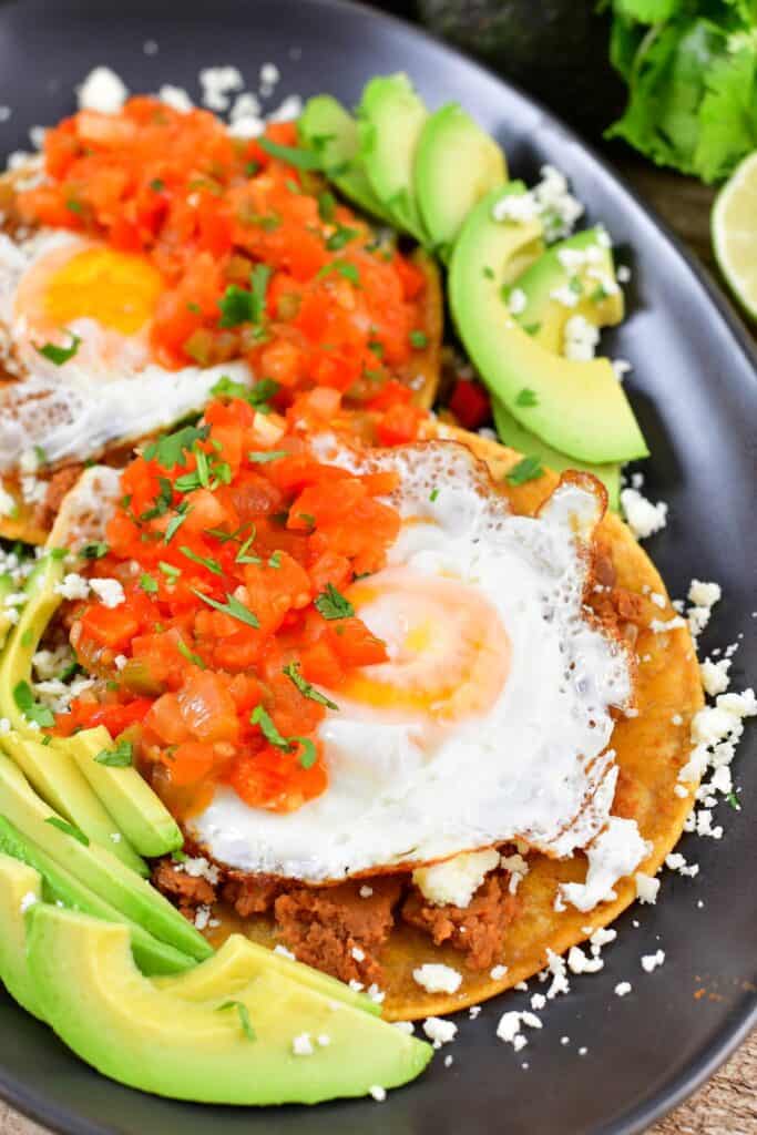 closeup of sunny side eggs over tortilla, beans, avocado