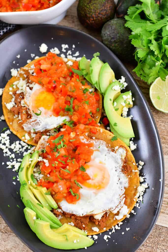 top view of huevos rancheros with toppings and avocadoes around