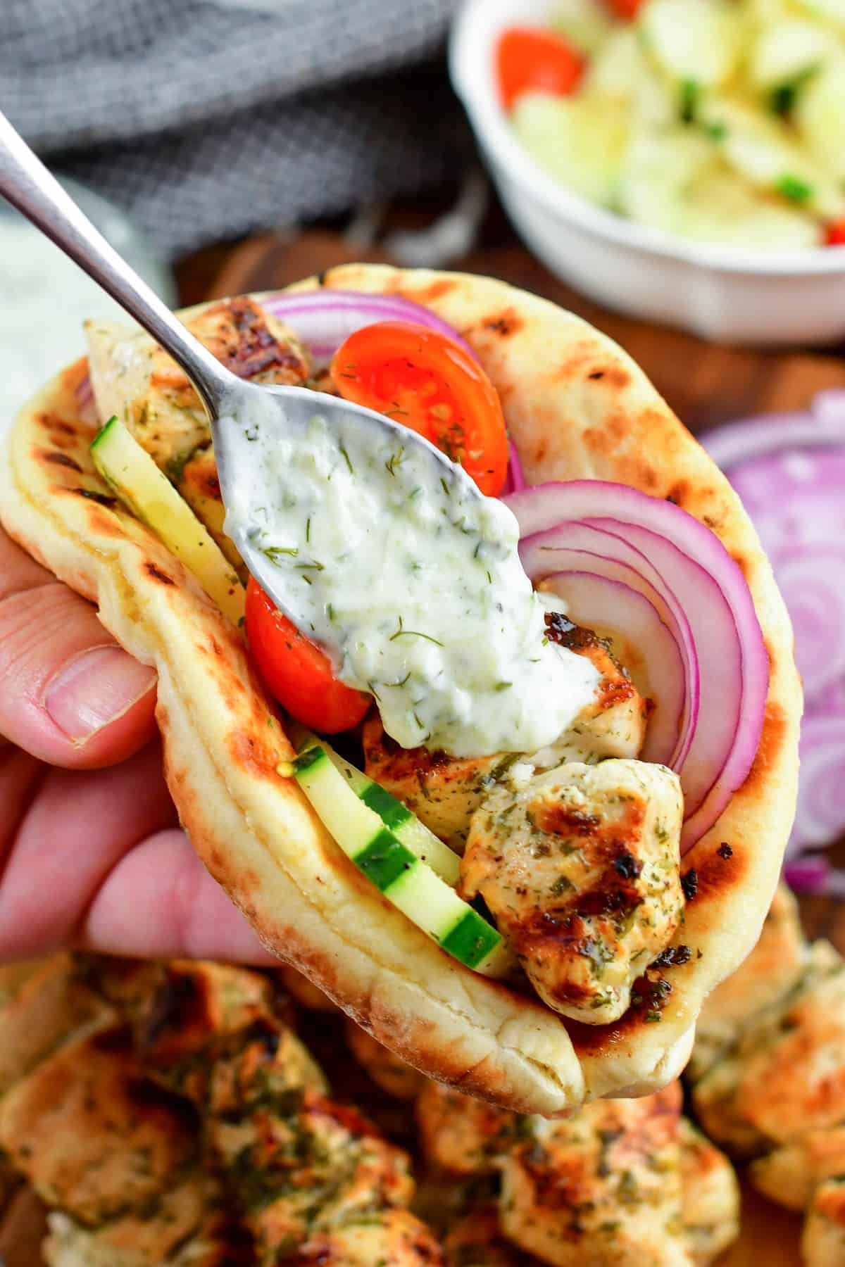 adding tzatziki sauce to chicken souvlaki in a pita