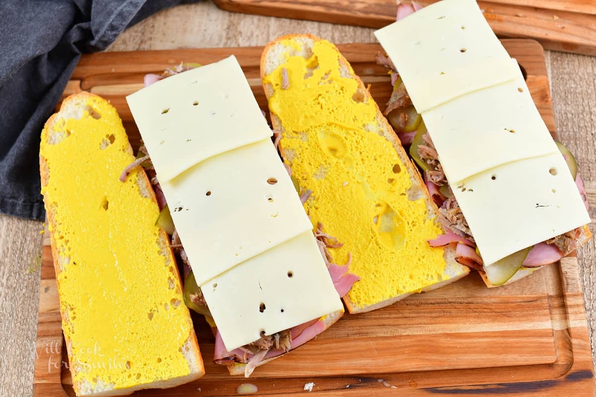 four sliced of long bread with mustard and meats on two with cheese.