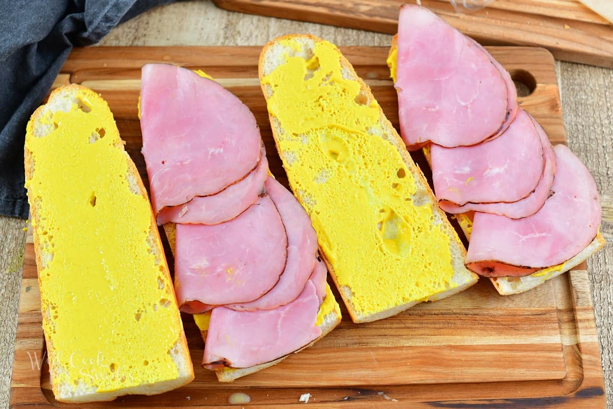 four slices of bread with mustard and ham on two.
