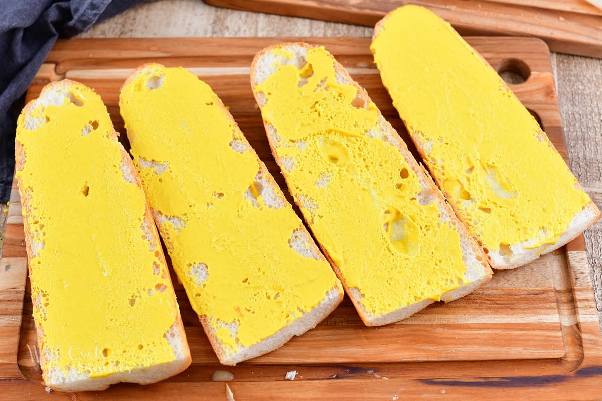 four halves of Cuban bread brushed with mustard.