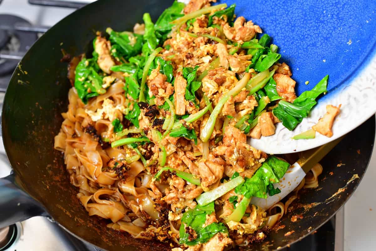 adding veggies and chicken back to the wok with noodles