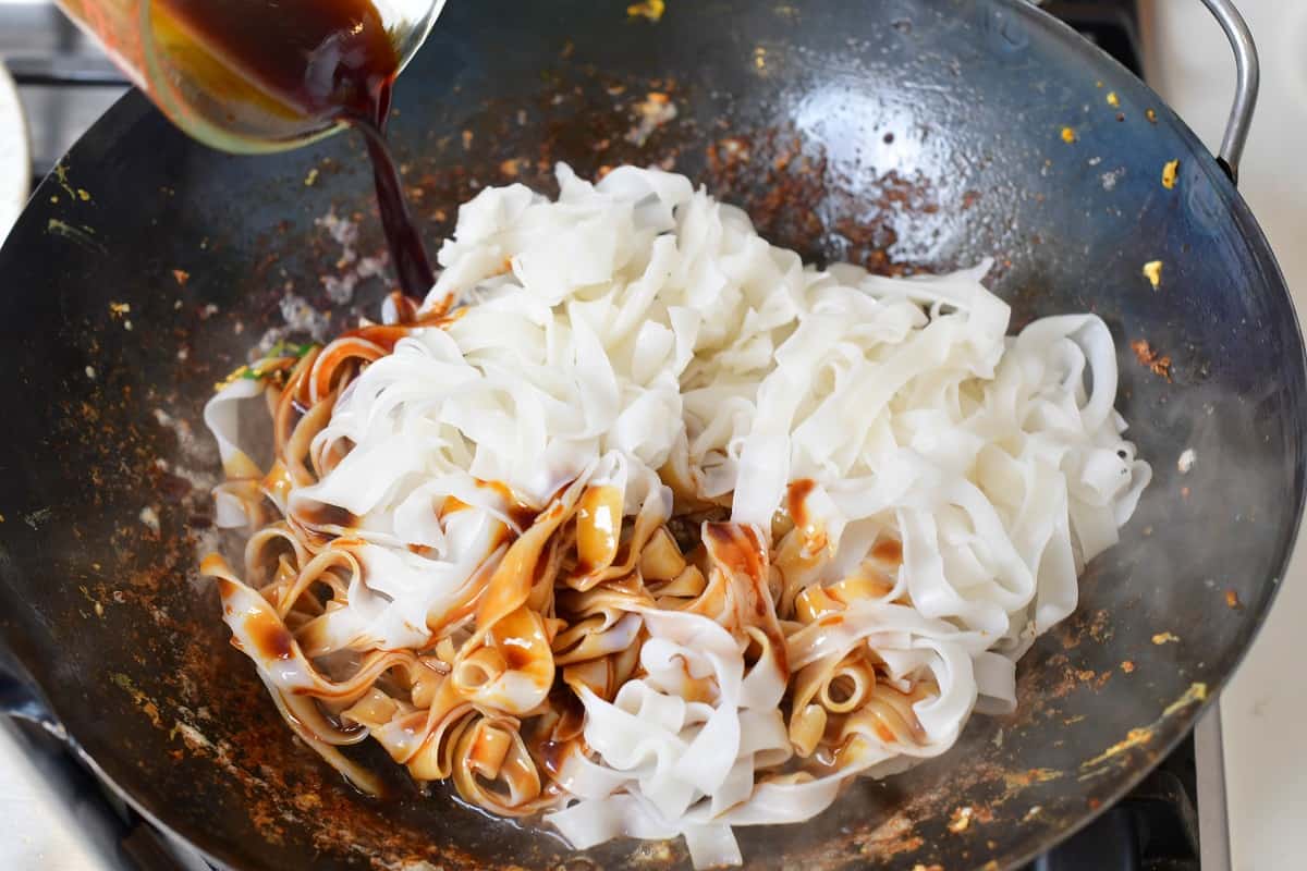 adding sauce to the rice noodles in wok