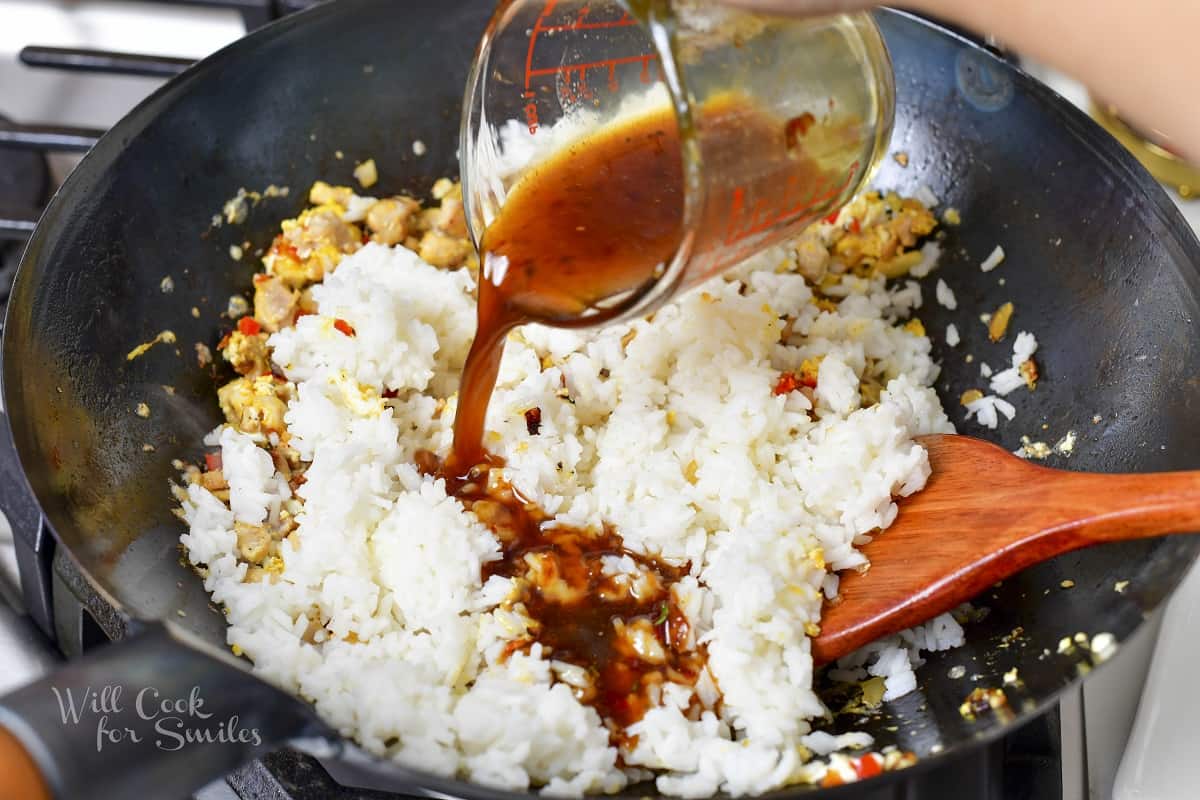 adding the sauce to the rice egg and veggies in wok