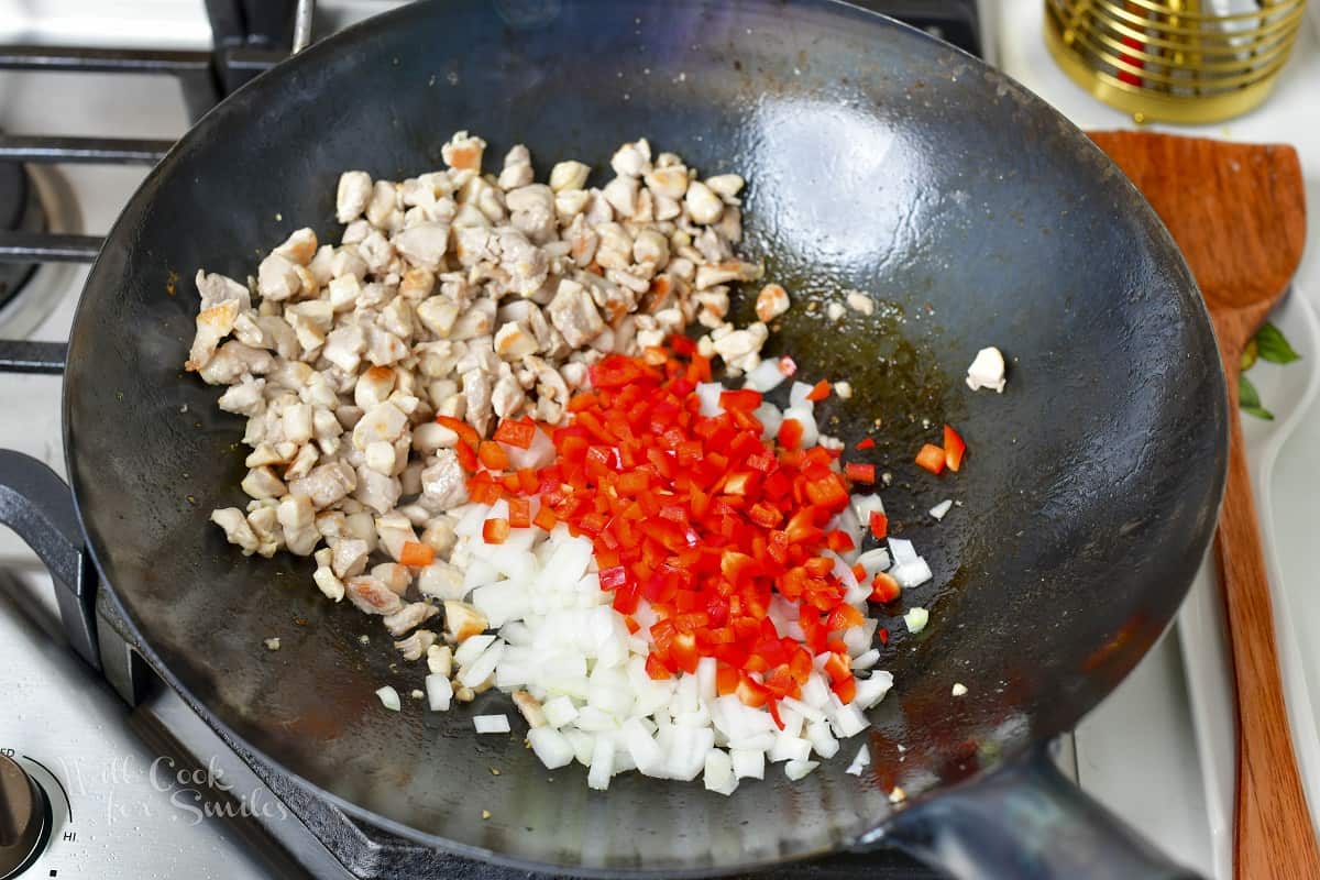 adding diced onions and pepper to the wok with chicken