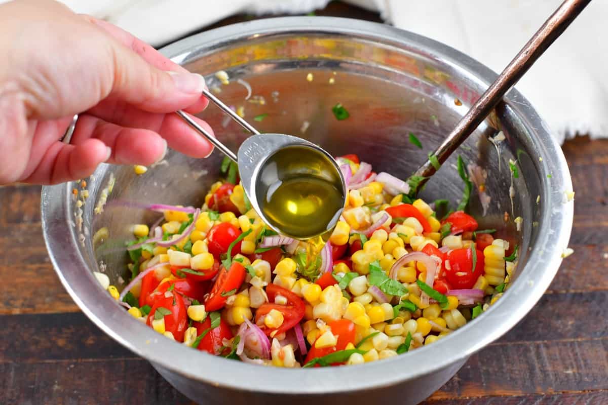 adding olive oil to the bowl with corn salad