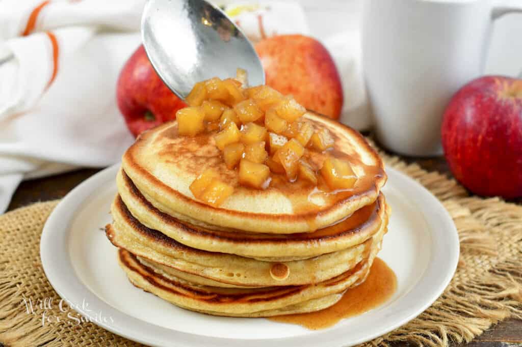 adding apple topping to the stack of pancakes