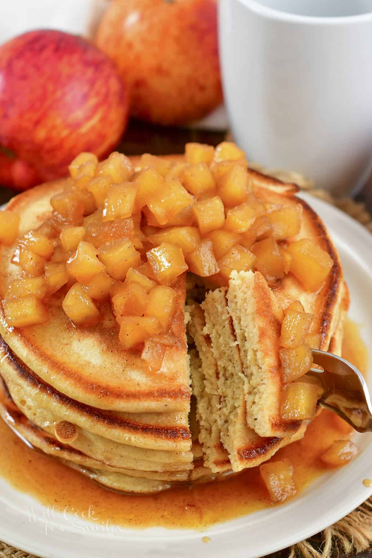 cutting into the stacked pancakes with apple topping