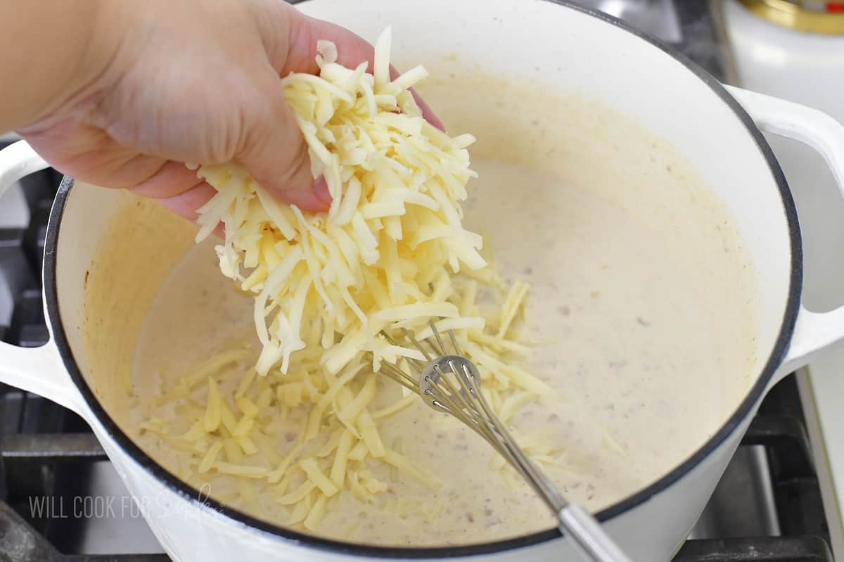 adding shredded white cheese to the pot with cream sauce.