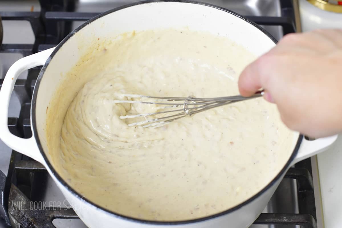 stirring the thickened creamy cheese sauce in a pot.