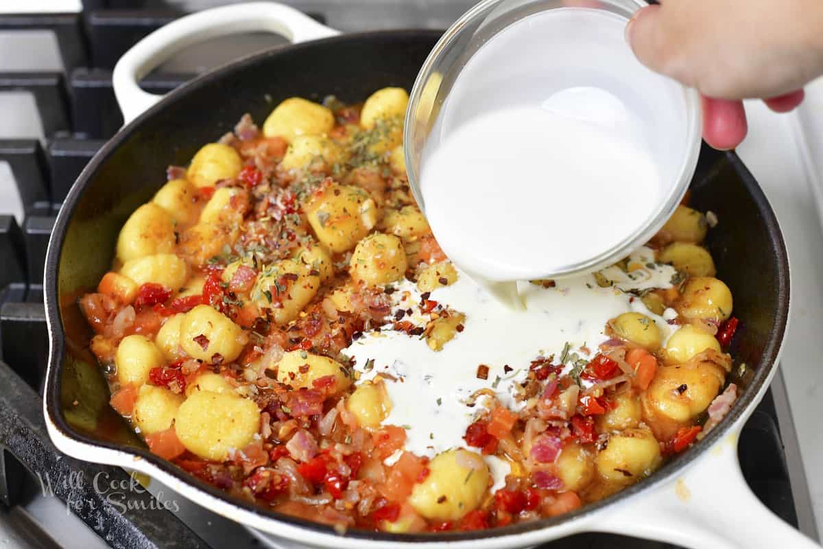 pouring in heavy cream into the pan with gnocchi