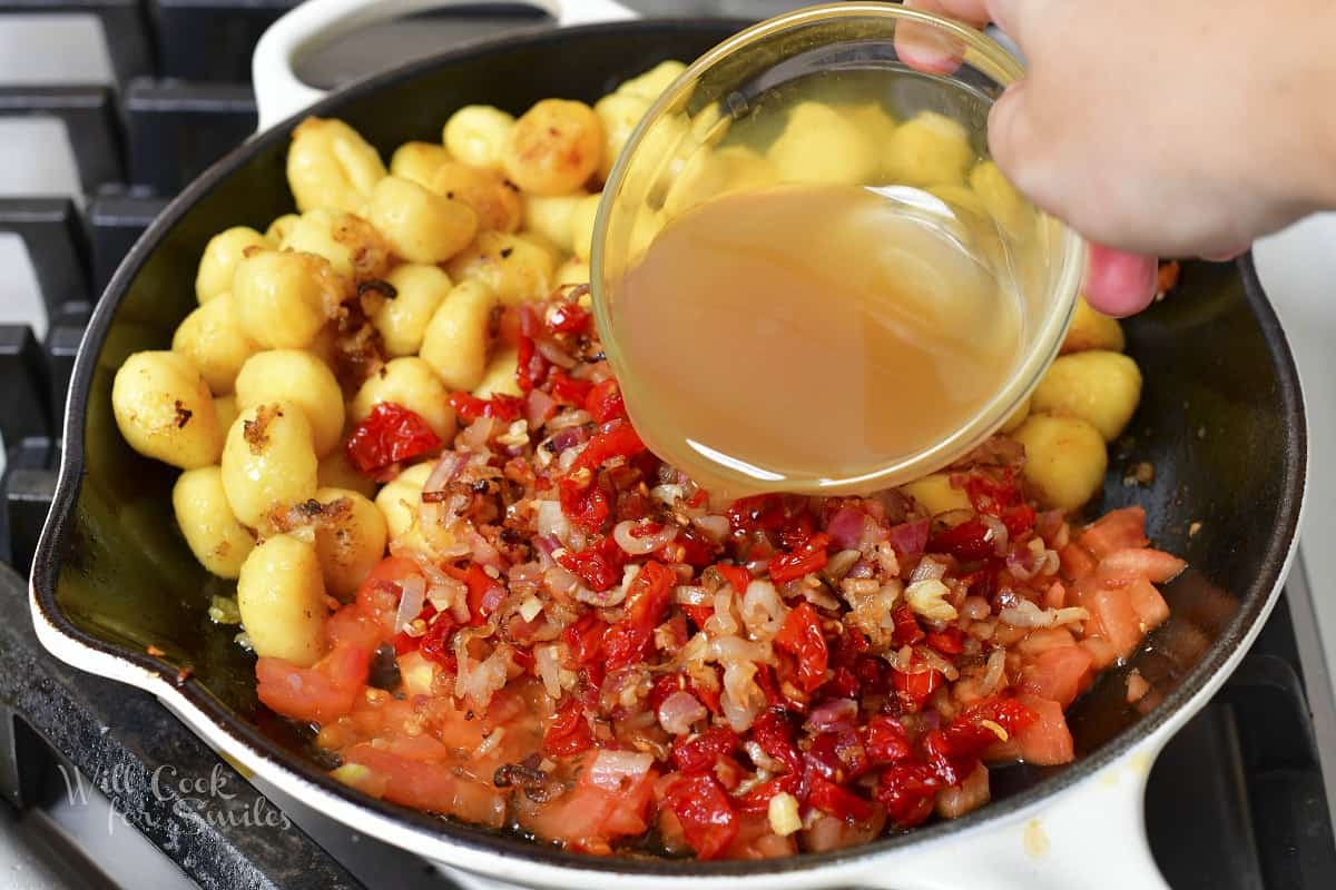 pouring in chicken stock into the pan with other ingredients