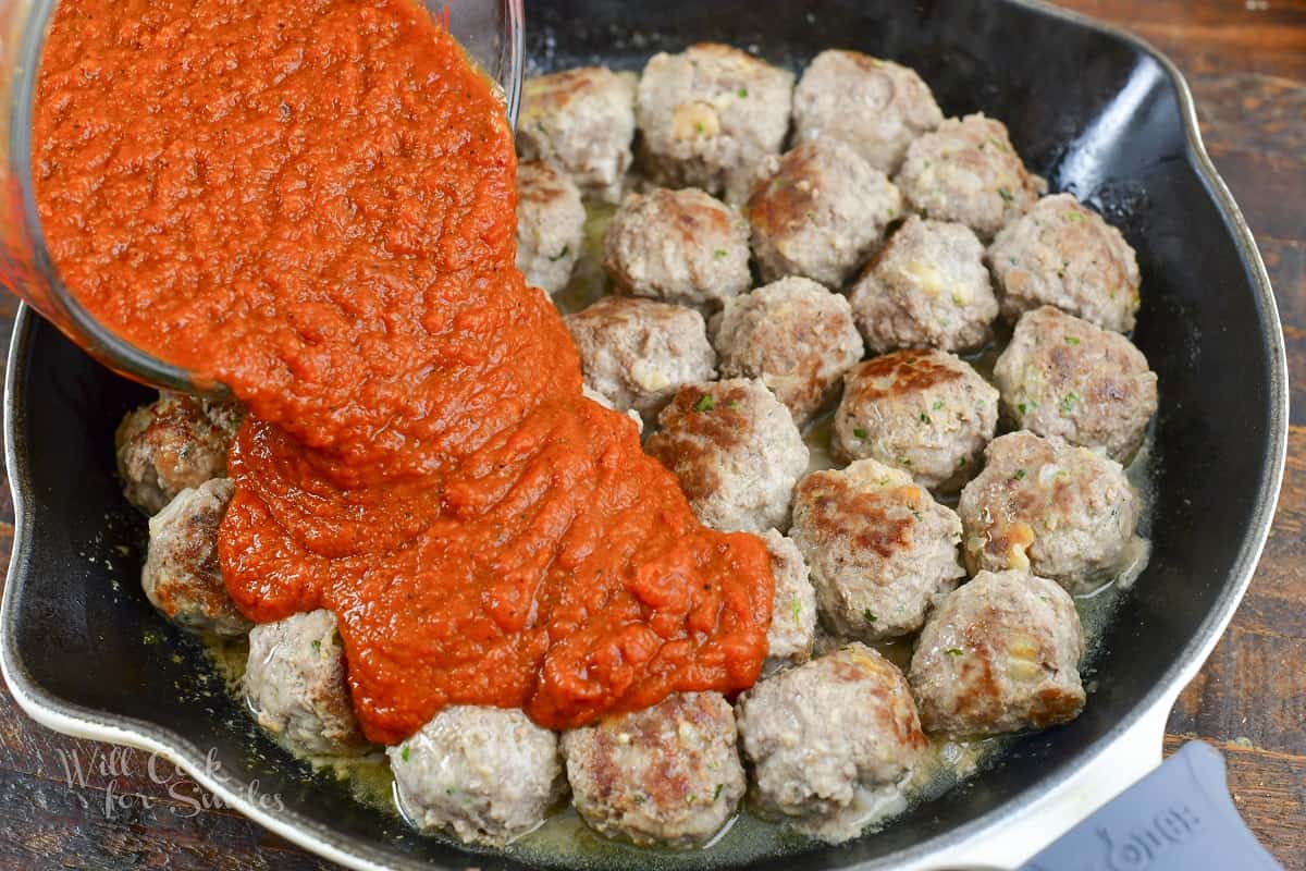 adding tomato sauce to the seared meatballs