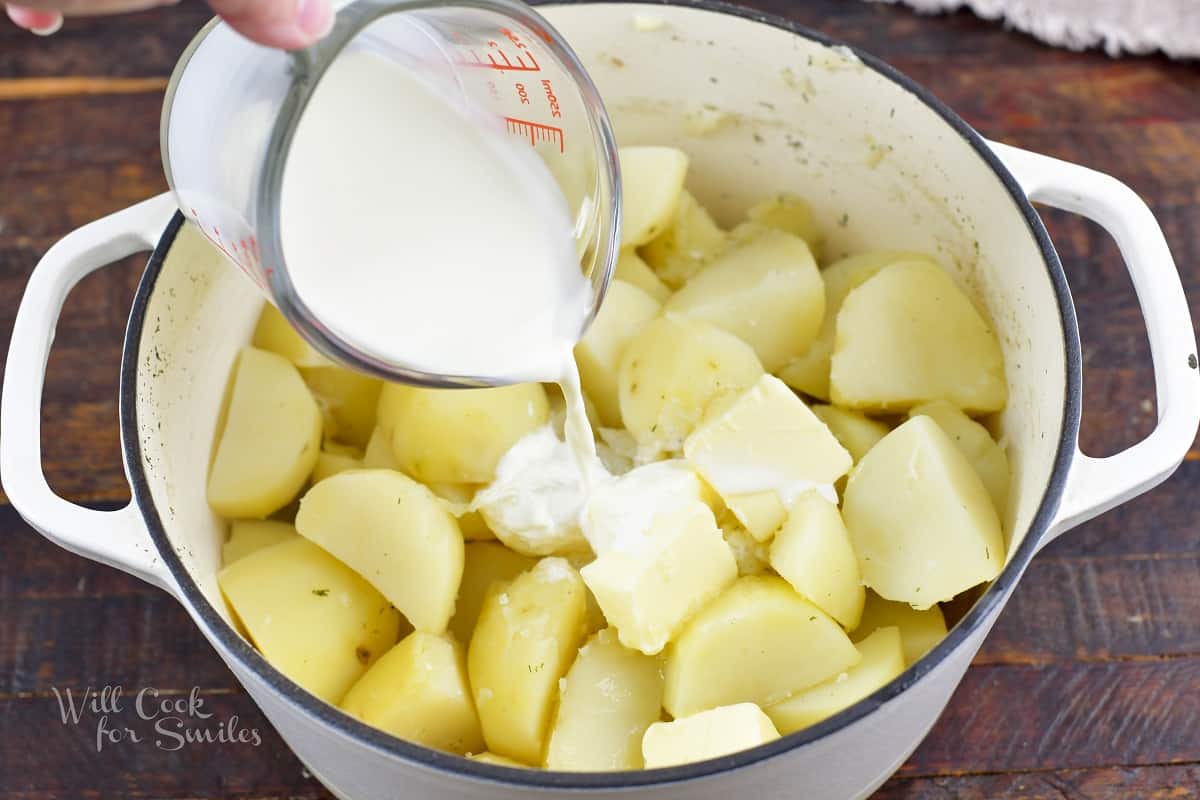 adding heavy cream to the cooked potatoes in a pot.