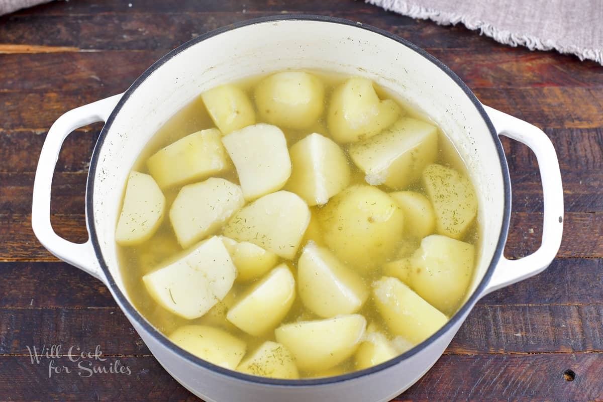 cooked potatoes in water in a white bowl.