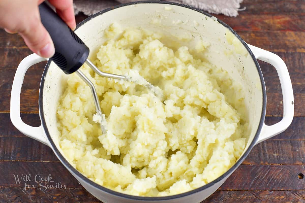 mashing potatoes in a white pot.