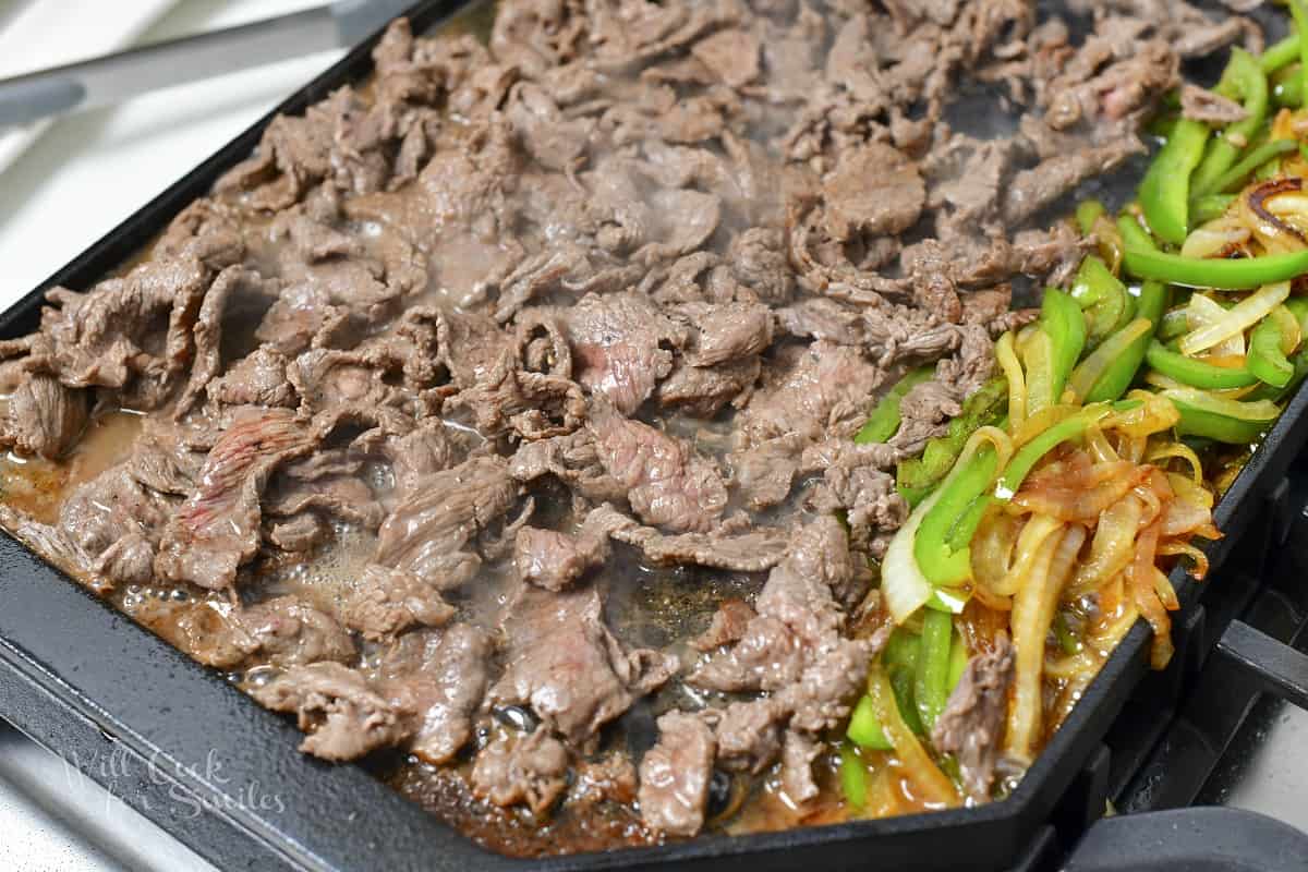 searing steaks next to onions and peppers