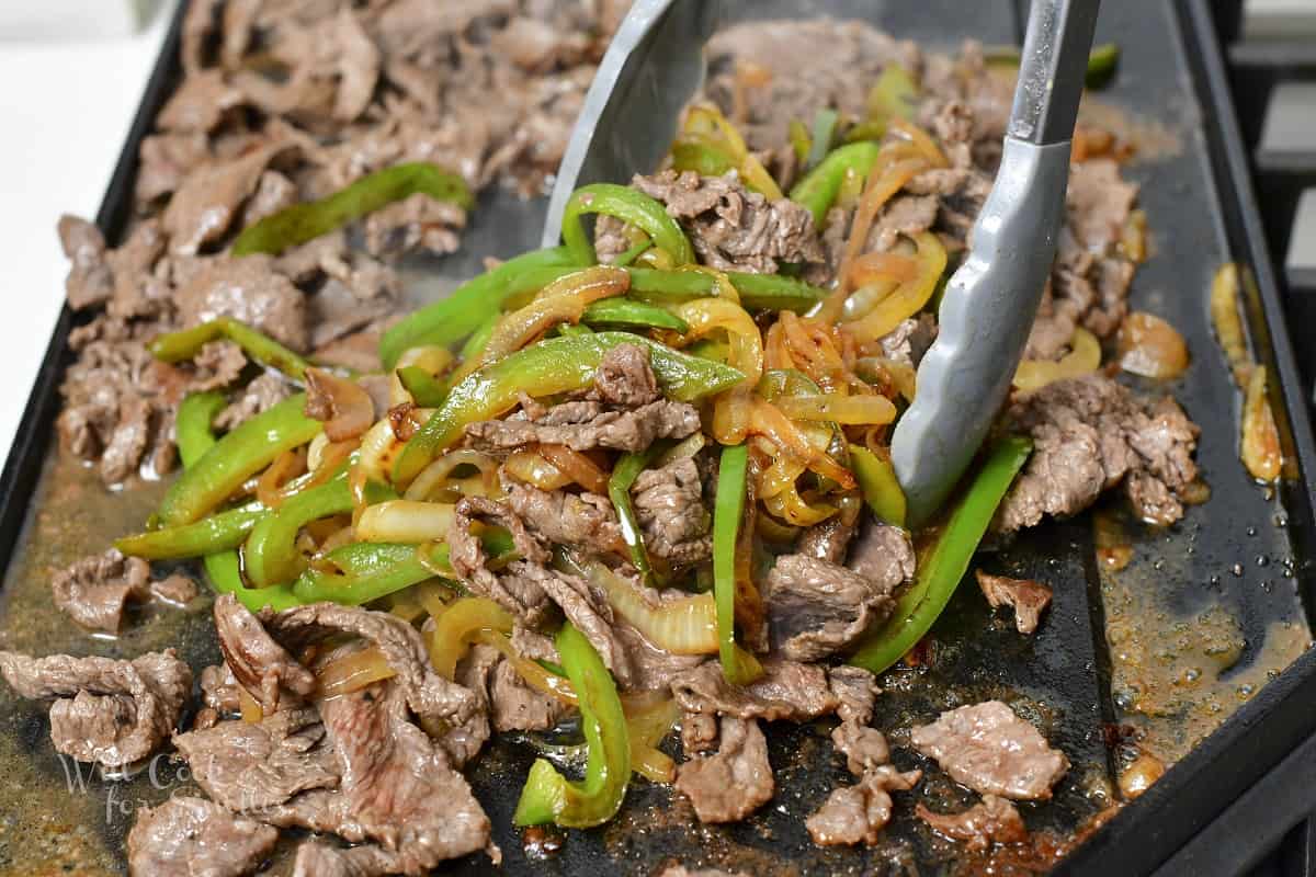 mixing onions, peppers, and steaks on the griddle