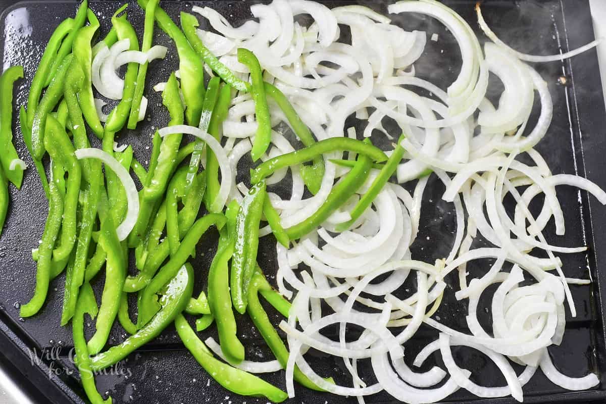 onions and green peppers searing on the griddle