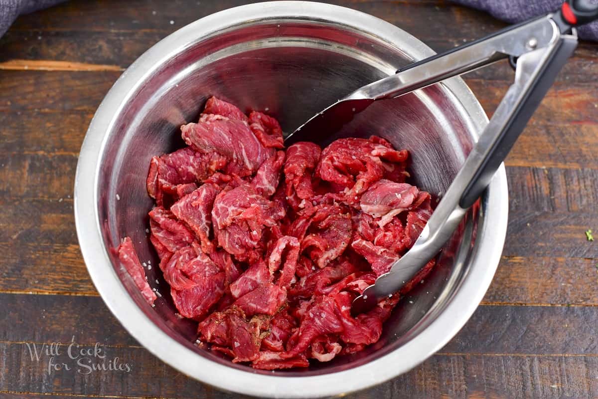 mixing thinly sliced steak with seasoning in a bowl