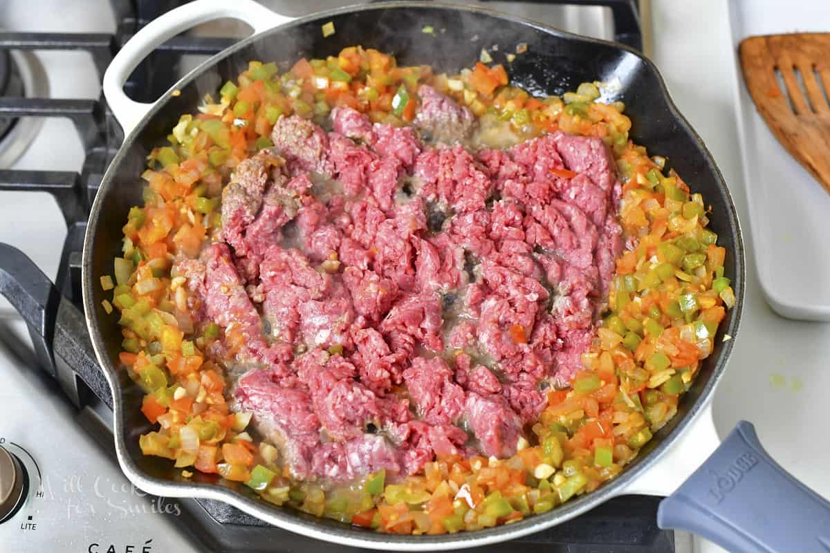 adding ground beef to the vegetables in the pan