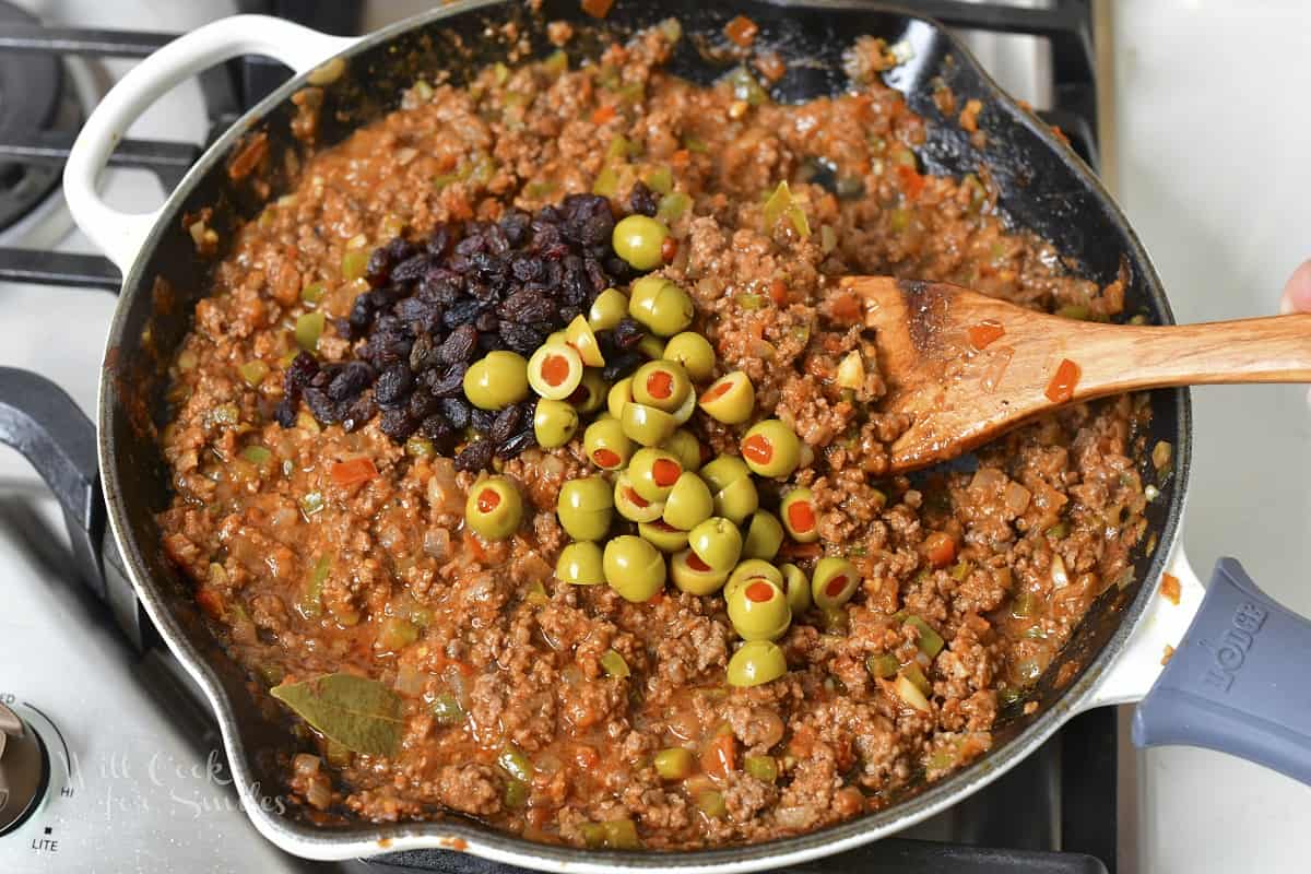 adding olives and raisins to the meat mixture in the pan