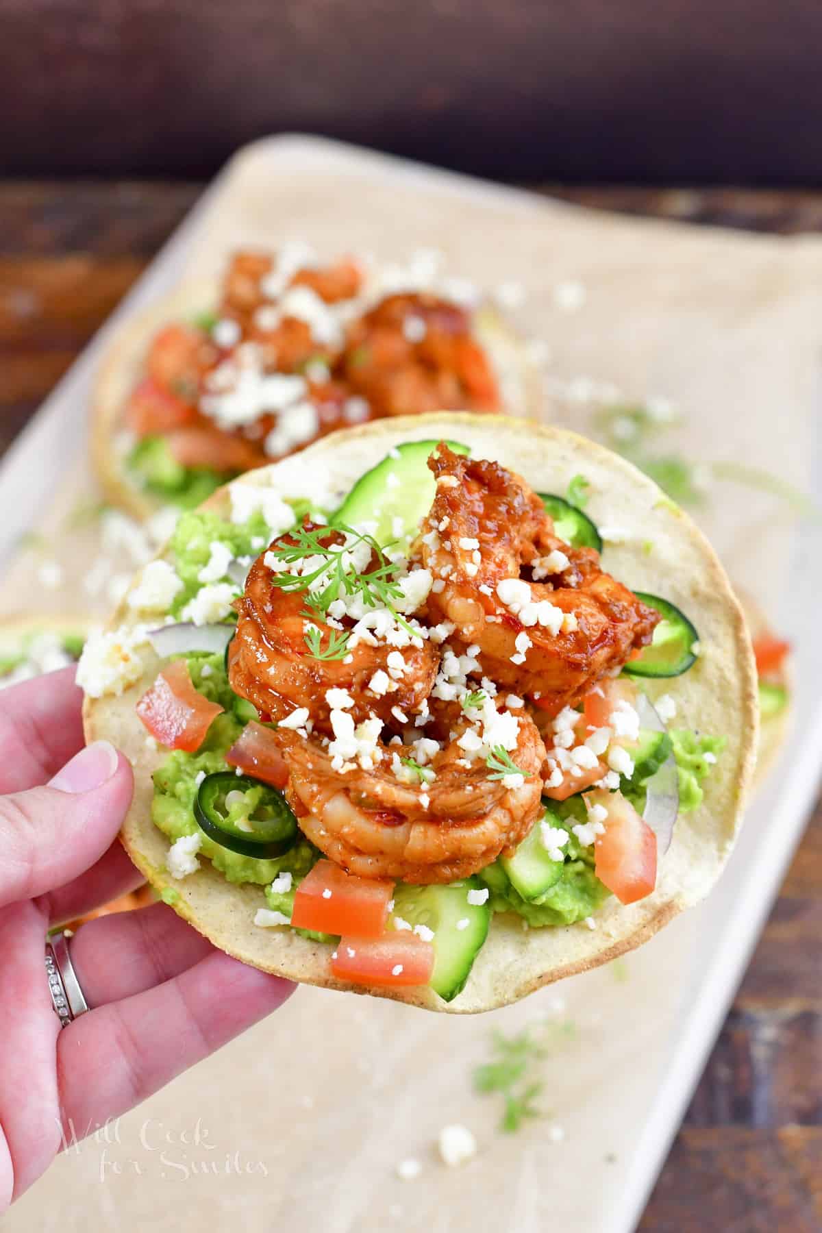 holding one tostada topped with shrimp and veggies