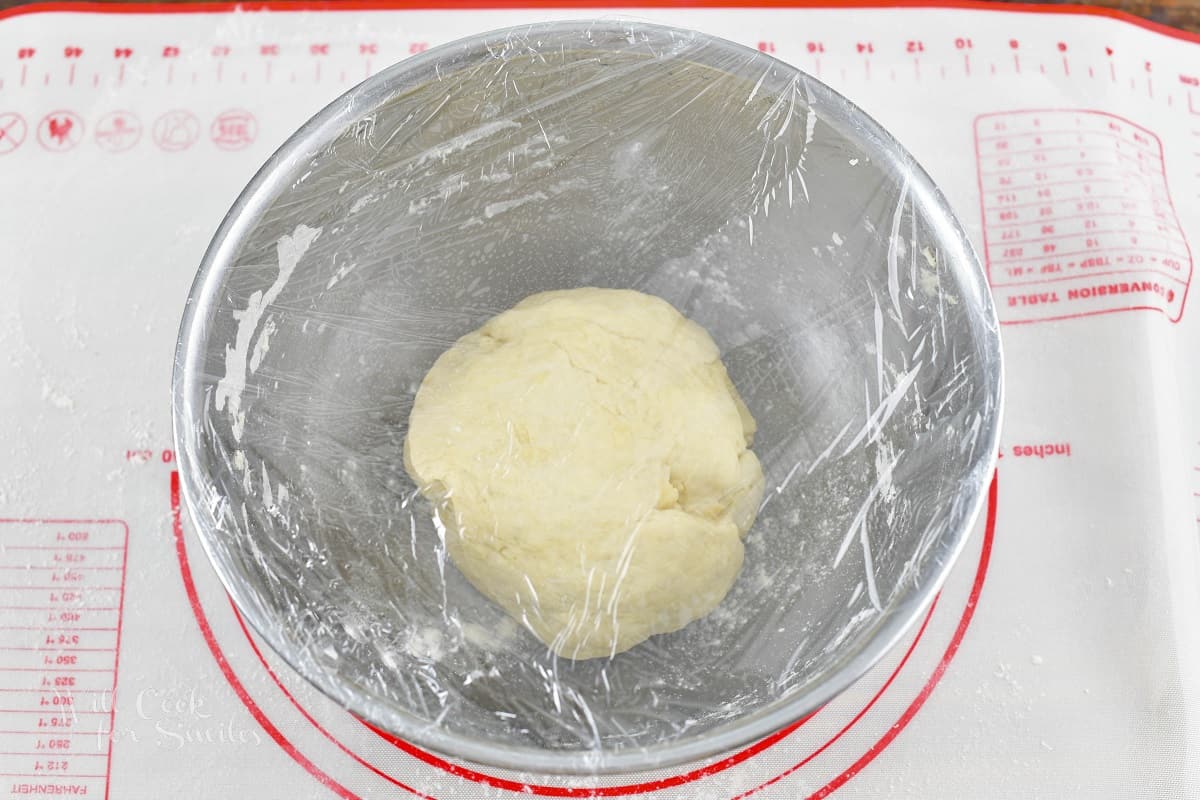 dough in the mixing bowl covered with plastic.
