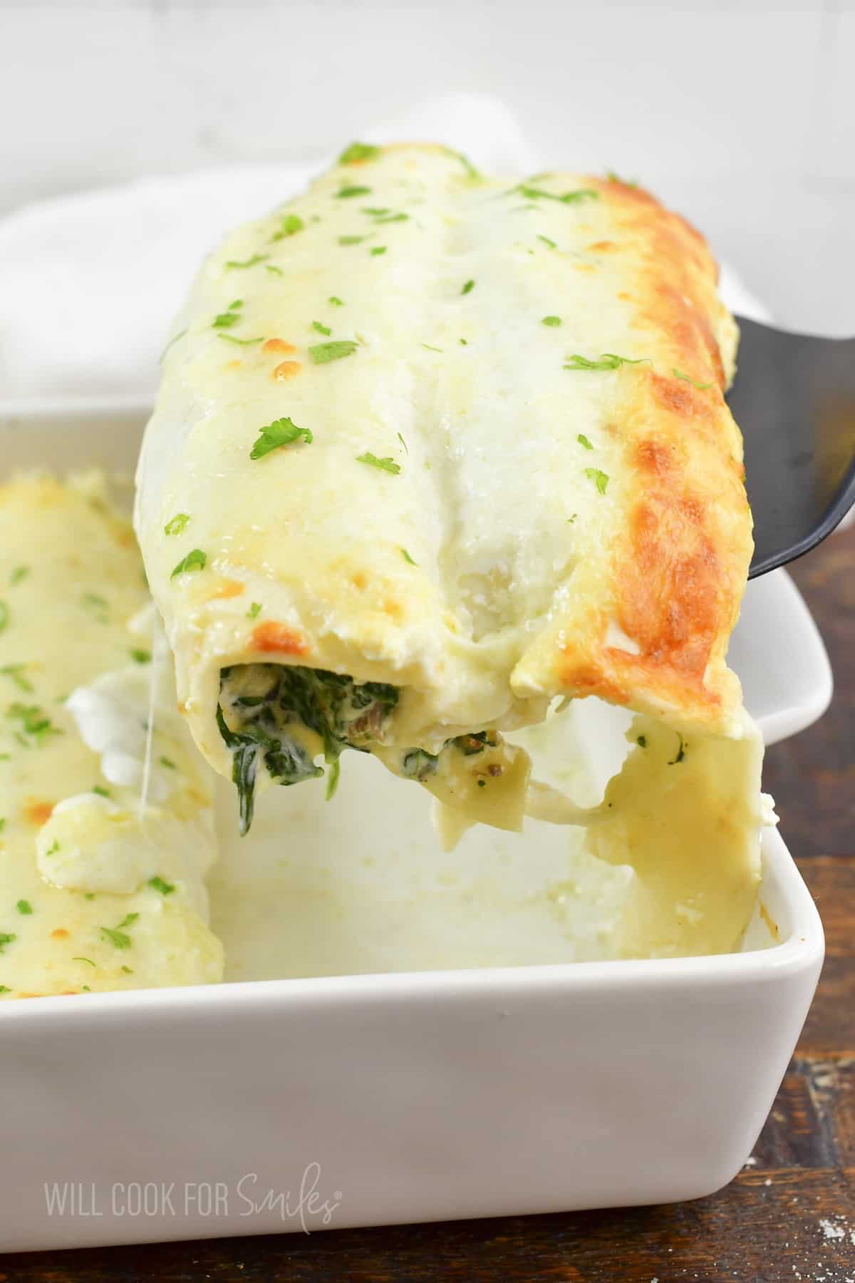 pulling out two enchiladas out of the baking dish.