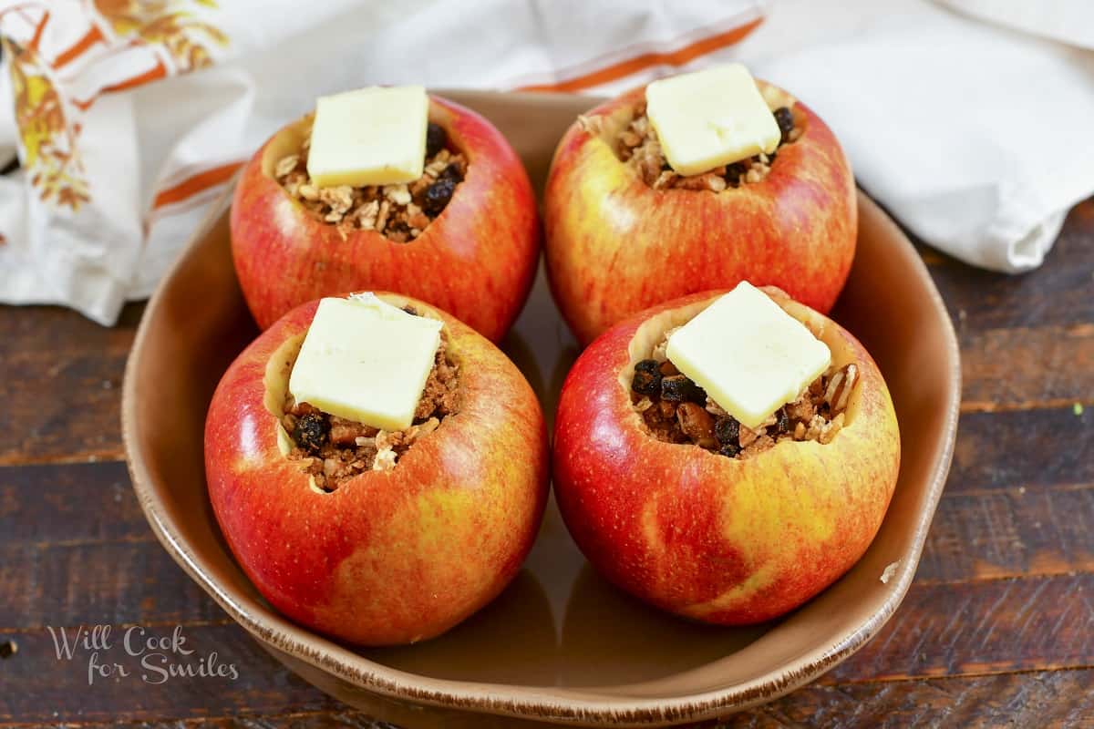 four filled apples in a baking dish with butter on top