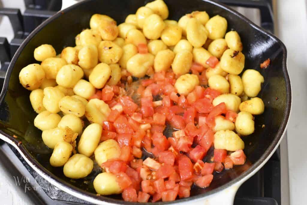 adding diced tomatoes to the gnocchi in the pan
