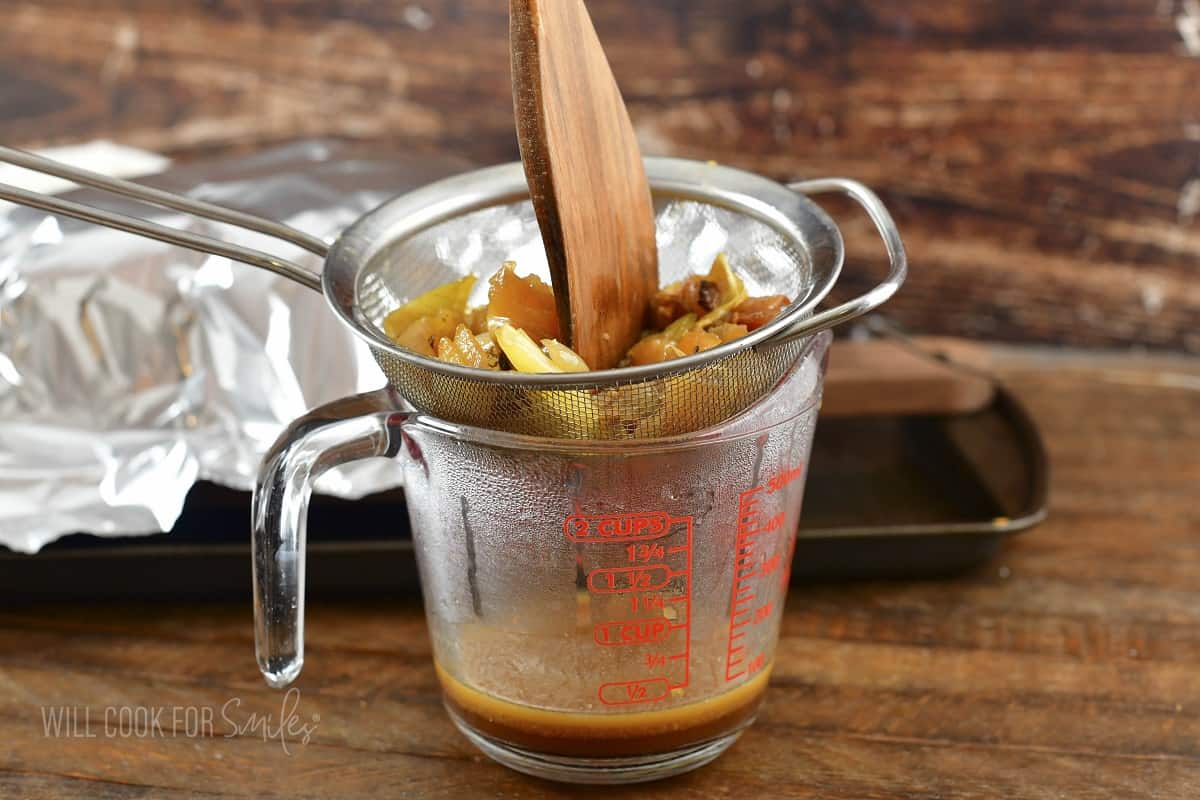 straining pan drippings and veggies into measuring cup.