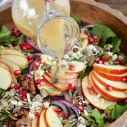 pouring the apple cider vinaigrette over salad.