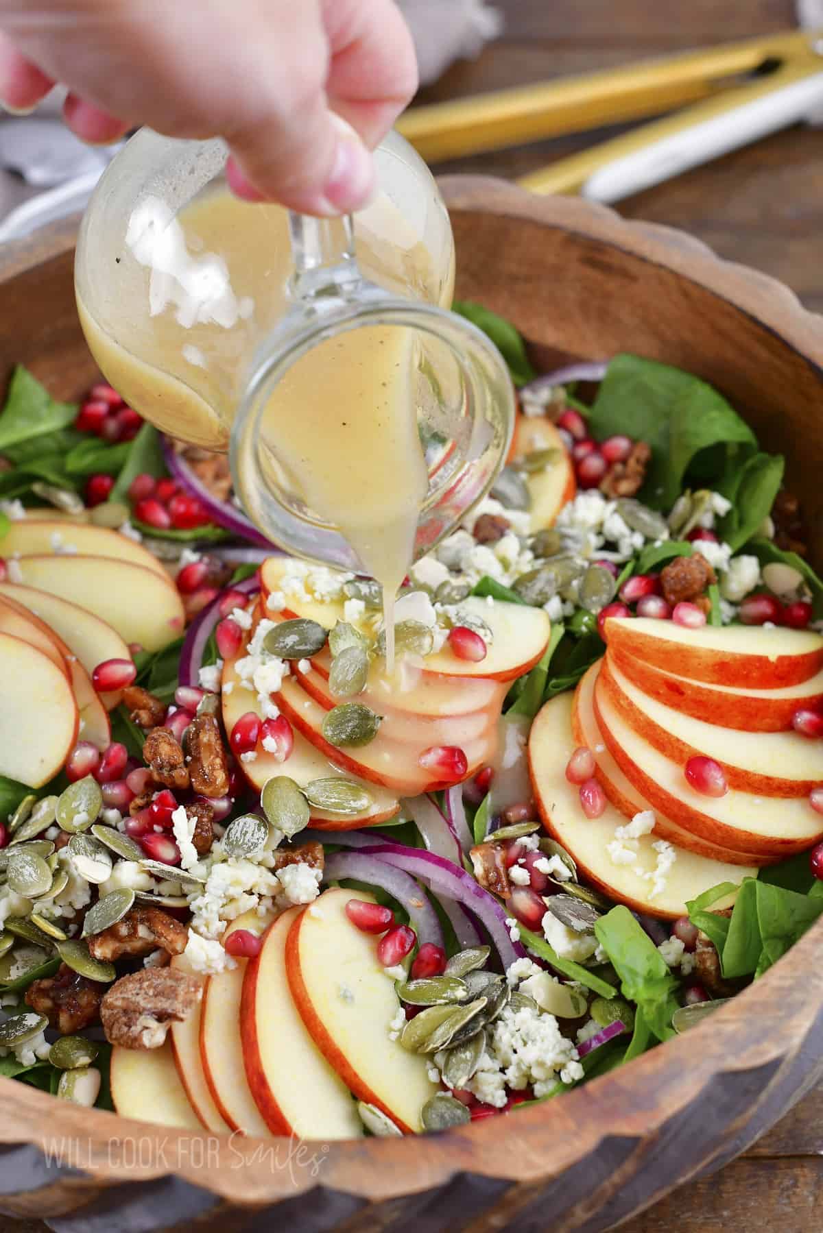 pouring the apple cider vinaigrette over salad.