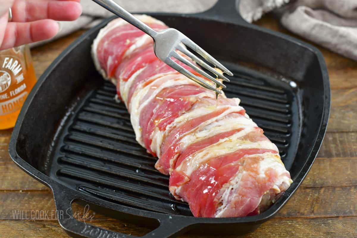 drizzling honey with a fork over bacon wrapped pork.