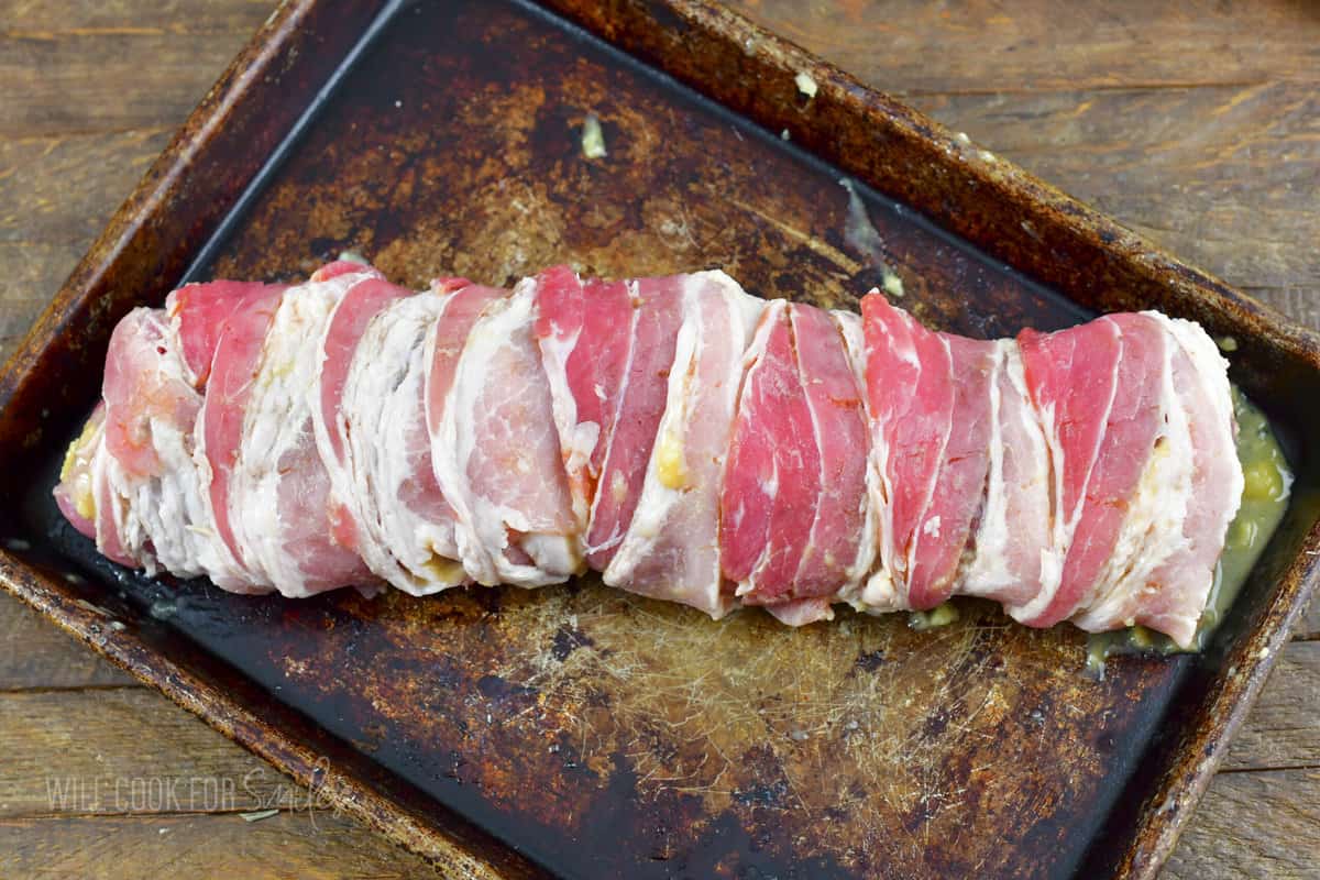 uncooked bacon wrapped pork on baking sheet.