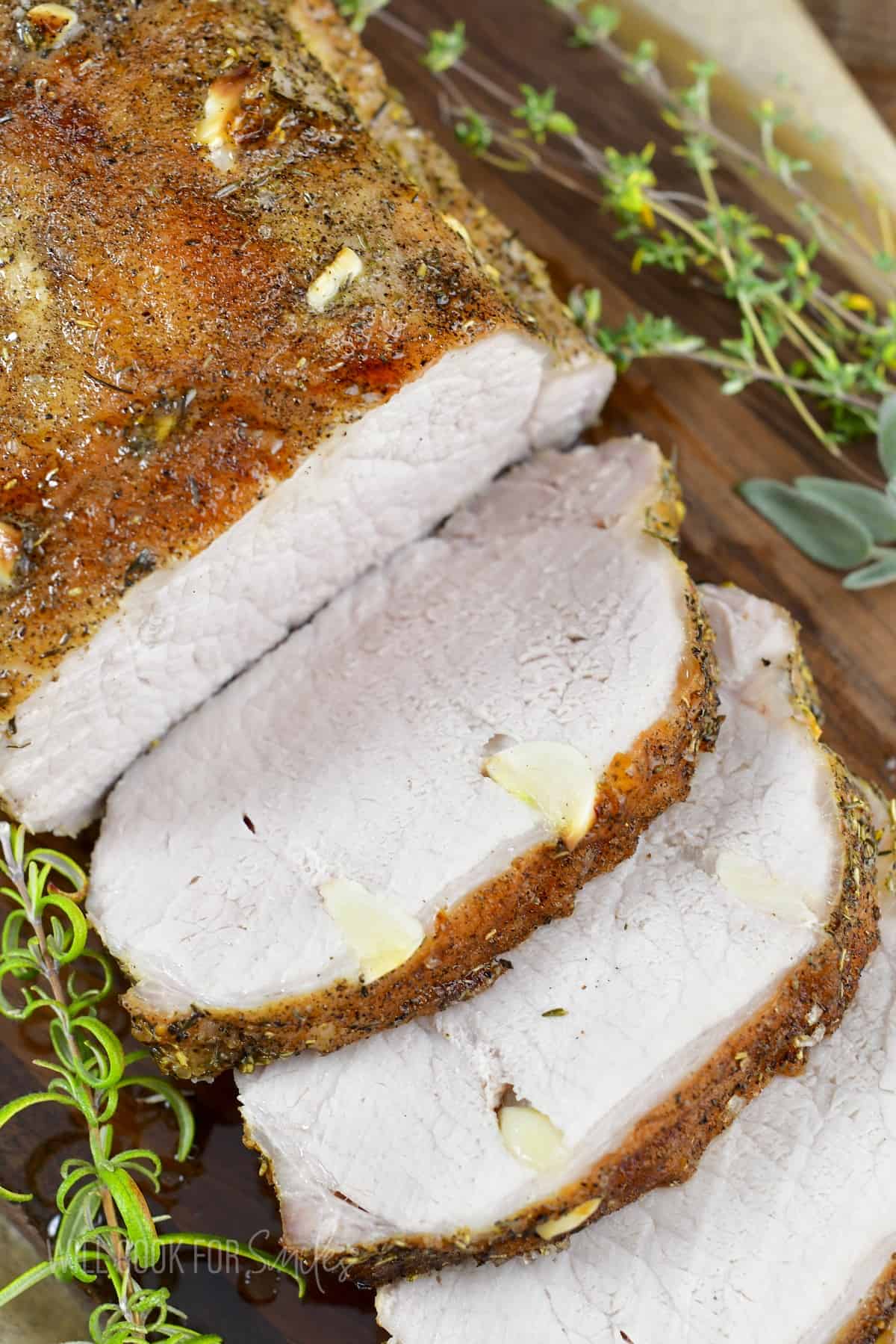 closeup of sliced garlic pork loin on the board with herbs.