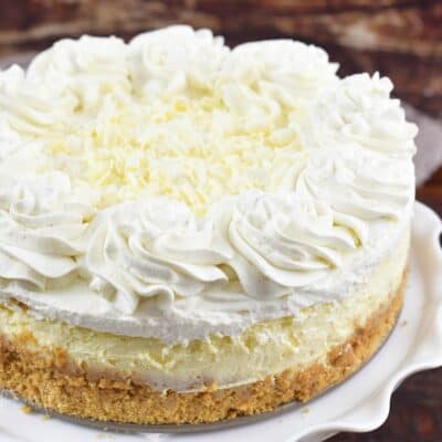 closeup whole vanilla cheesecake with whipped cream.