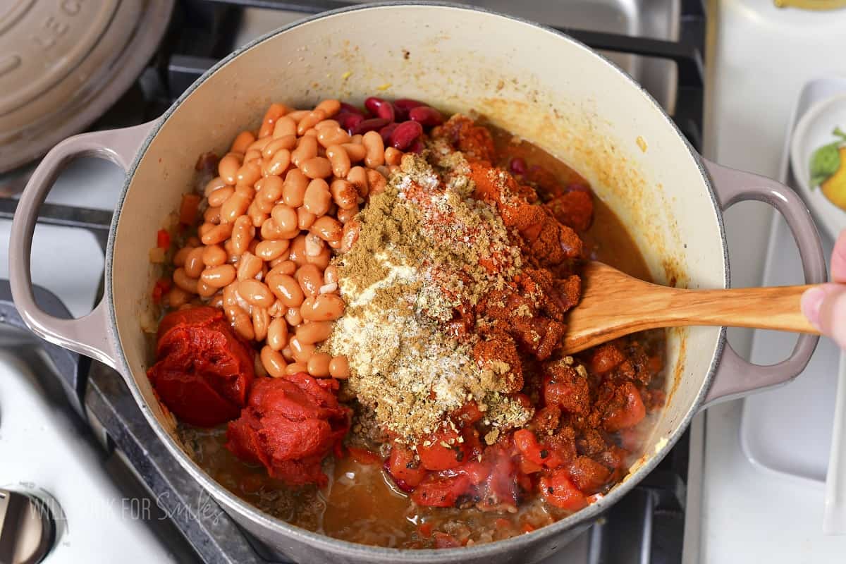 adding beans, tomatoes, and seasoning to the chili.