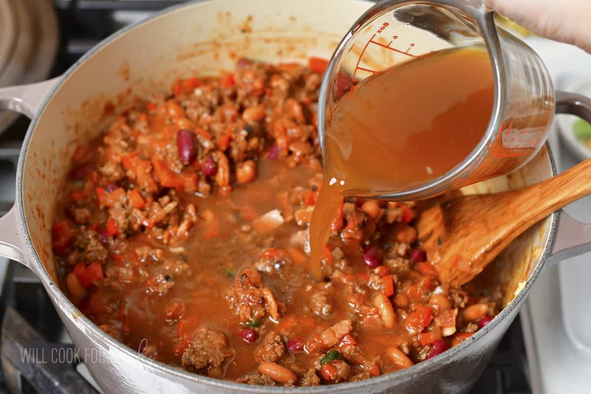 adding beef stock to the chili in the pot.