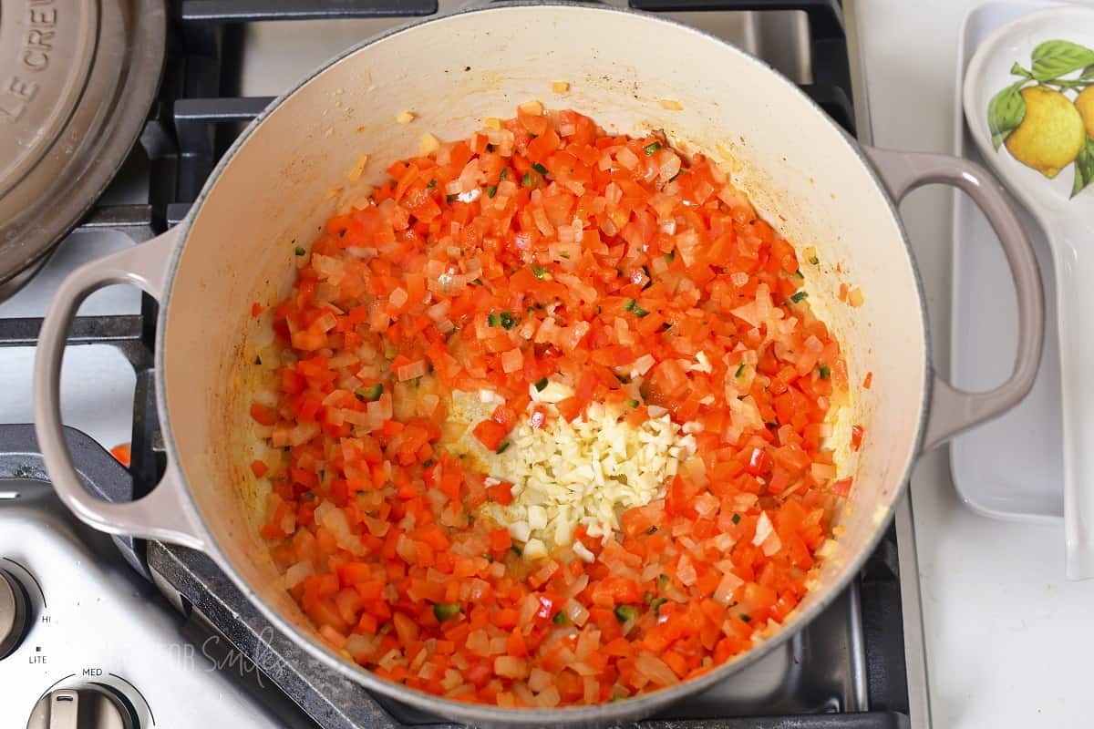 adding minced garlic to the softened veggies in a pot.