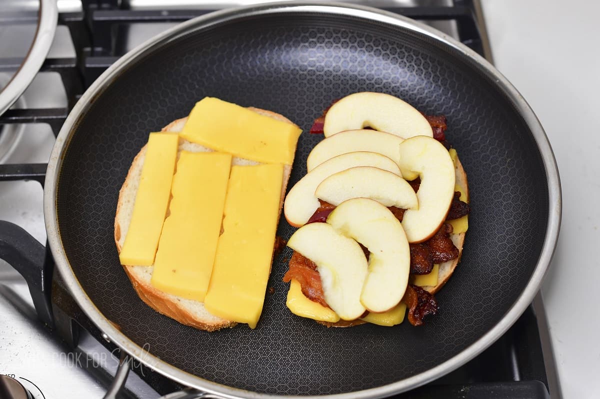 two slices of bread in a pan with cheese and one with bacon and apple.